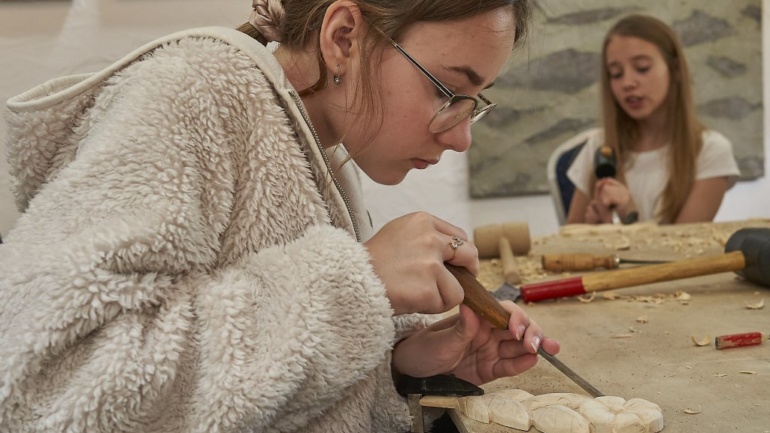 Zdjęcie przedstawia dziewczynę króra rzeźbi w drewnie